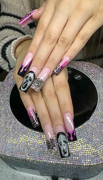 A high-angle photograph displays long, square-shaped nails with elaborate Halloween-themed designs, including pink dripping polish, spiderweb patterns, and silver glittery "Scream" masks.