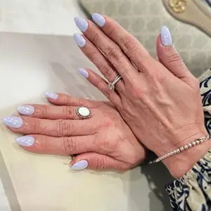 A close-up photograph features hands with almond-shaped nails finished in a soft, glossy pale lavender or periwinkle polish.