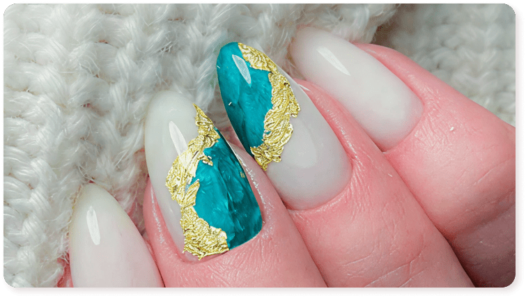 Close-up of decorative nail art featuring white, turquoise, and gold leaf foil.