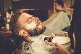 Man lying back in a salon chair with white shaving cream on his face.