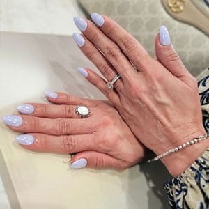 A close-up photograph features hands with almond-shaped nails finished in a soft, glossy pale lavender or periwinkle polish.