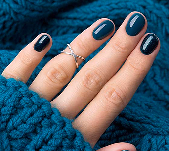 Hand with a silver "X" ring and glossy teal-blue manicured nails resting on a blue knit sweater.